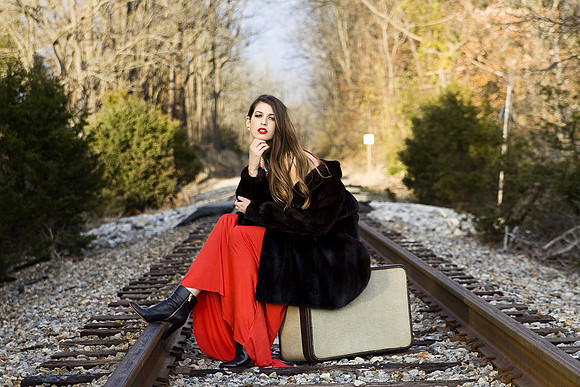 Fashoin photograph of woman in red dress with fur coat on railroad tracks